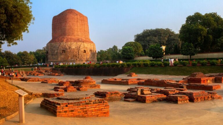 Dhamekh-stupa in sarnath im warmen abendlicht, ort der ersten lehrrede des buddha, davor die freigelegten ziegelfundamente der klosteranlage