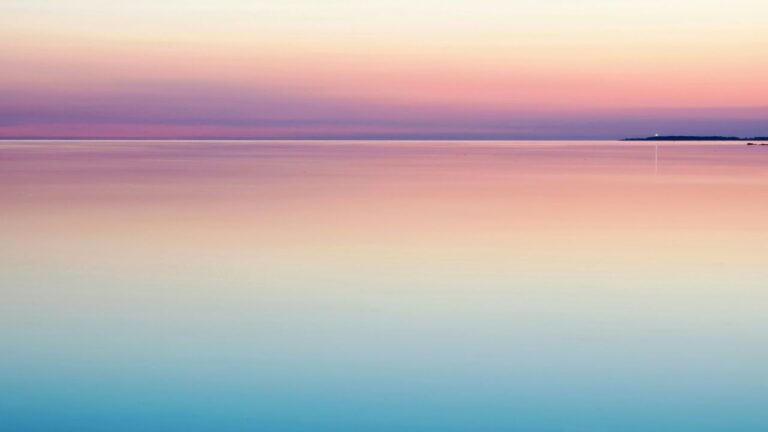 Ruhige wasserfläche im dämmerlicht als beitragsbild zur wirkung von meditation, am horizont ein landstreifen mit einem einzelnen licht